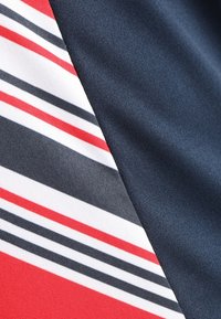 Námořnická modrá tkanina s hladkým povrchem má červené, bílé a černé horizontální pruhy v diagonální sekci. Jasný barevný kontrast.