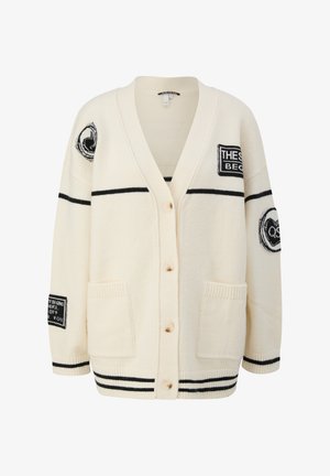 Cream cardigan with black stripes, button closure, patch pockets, and multiple black and white graphic patches on sleeves and chest.