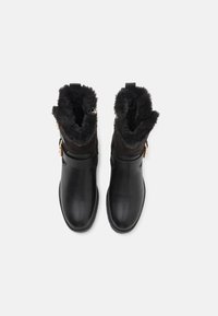 Svarta läderankelboots med fluffigt svart foder, utrustade med spänndetalj och slät, snygg yta. Stängd tå-design.