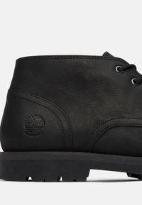 Stivale alla caviglia in pelle nera con texture liscia, forma rotonda e design con lacci. Presenta un marchio impermeabile e una suola robusta.