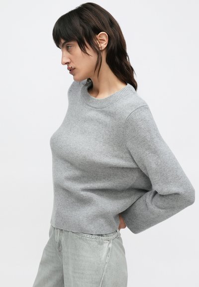 Ανοιχτό γκρι πλεκτό πουλόβερ με στρογγυλή λαιμόκοψη και ριμπ μανσέτες. Το ύφασμα φαίνεται απαλό, με άνετη εφαρμογή και ελάχιστες ραφές.