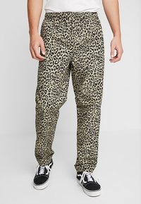 Leopard print pants in beige and black fabric, featuring an elastic waistband and straight, wide legs. Paired with black sneakers.
