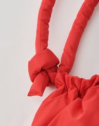 Borsa rossa con spallacci imbottiti annodati e parte superiore arricciata. Il materiale sembra liscio, senza modelli visibili o dettagli in metallo.