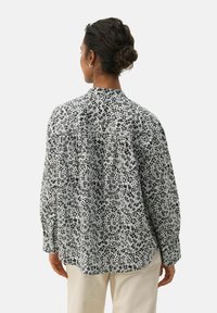 Camicia a maniche lunghe con stampa floreale bianca e nera, caratterizzata da un collo alto, pieghe e una vestibilità morbida, realizzata in tessuto leggero.