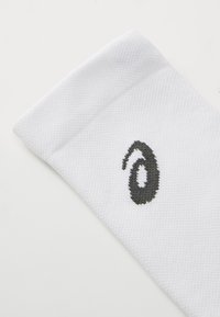 Weißer Sportsock mit einem strukturierten Strickmuster und einem schwarzen Logo an der Seite. Verfügt über einen gerippten Bund für einen guten Sitz und Komfort.