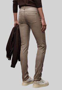 Pantalones ajustados beige con una textura suave, que cuentan con bolsillos traseros y detalles laterales, combinados con una chaqueta bomber marrón y zapatillas blancas.