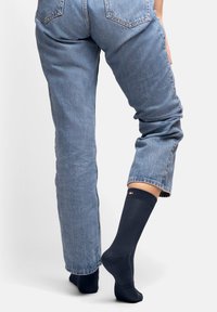 Mörkblå bomullssockor med ribbad kant, som bärs med ljusblå uppvikta jeans. Har en liten logotyp nära toppen.