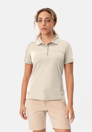 Helles beiges Polo-Shirt mit Kragen, drei Knöpfen und kleinem Logo. Der Stoff wirkt glatt und leicht. Getragen mit beigen Shorts.