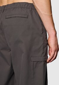 Grå cargobyxor med elastisk midja, sidofickor och ett texturerat tyg. Har en ficka på baksidan för ytterligare användbarhet.