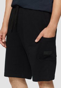 Zwarte shorts van katoen, met een elastische tailleband, zijzakken en een natuurgetrouwe patch op de rechterzak.