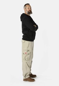 Zwarte hoodie, beige cargobroek en bruine laarzen. De cargobroek heeft zakken en een logo patch, terwijl de hoodie een klassiek ontwerp heeft.