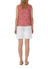 Rode gestippelde mouwloze top met een wit diamanten patroon, gecombineerd met witte shorts met omgeslagen zoom. Platte sandalen maken de outfit compleet.