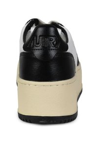 Sneaker in pelle bianca e nera con una suola spessa color crema. Presenta un logo nero in rilievo sul tallone. Texture liscia con colori a contrasto.