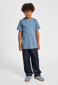 Ljusblå bomulls-T-shirt med korta ärmar, kombinerad med mörkblå jeans. Fodralet har blå och beige detaljer, med en logotyp på tröjan.