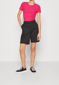 Strak aansluitend geribd roze topje met korte mouwen, gecombineerd met zwarte shorts tot op de knie en marineblauwe sneakers met witte zolen. De shorts hebben steekzakken aan de voorkant en een knoop.