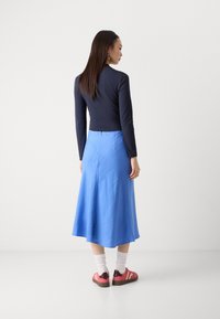 En langermet marineblå topp kombinert med en lys blå, flytende midiskjørt. Outfiten fullføres med rosa joggesko og hvite sokker.