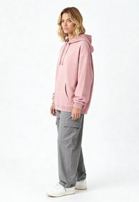 Felpa oversized di colore rosa chiaro con tasca a marsupio, polsini a costine e cappuccio con coulisse, abbinata a pantaloni cargo grigi e sneakers bianche.