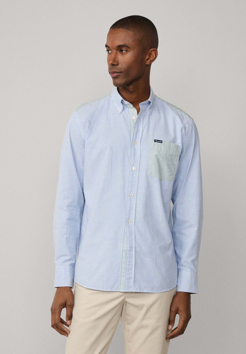 Camicia button-up a righe blu chiaro e bianco con una tasca di un verde uniforme. Presenta un colletto classico e maniche lunghe. Tessuto di cotone.