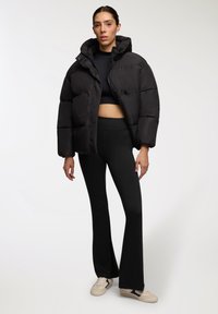 Czarna kurtka puchowa z kapturem, z pikowanym wzorem i bocznymi kieszeniami. Nosi się ją na czarny top crop i czarne spodnie z wysokim stanem.