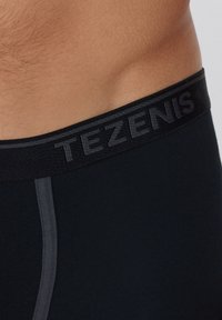 Schwarze Boxershorts für Männer mit einem strukturierten elastischen Bund, der das Logo "TEZENIS" in Dunkelgrau trägt, und einer glatten Stoffoberfläche.