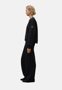 Sudadera negra corta con cuello redondo y mangas largas, combinada con pantalones negros anchos. Textura suave, diseño minimalista.