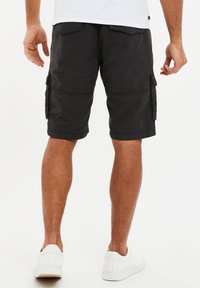 Bermudas negras de algodón, con múltiples bolsillos laterales y un corte relajado, combinadas con zapatillas blancas.