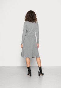 Abito grigio in maglia con maniche lunghe, corpetto aderente e gonna a pieghe svasata. Abbinato a stivaletti neri alla caviglia con tacco a blocco.