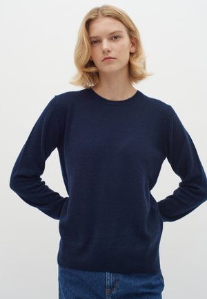 Suéter de punto azul marino con mangas largas, cuello redondo, dobladillo acanalado y textura suave, combinado con jeans de mezclilla azules.