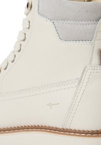 White leather high-top shoe featuring a smooth texture, gray suede accents, metal eyelets, and a stitched sole with a subtle logo.
