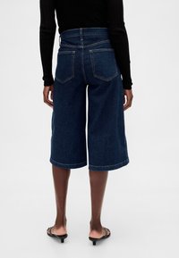 Blå denimculottes med hög midja, vida ben och rå fåll. Har två bakfickor. Kombineras med svarta sandaletter med klack.