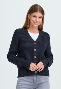 Cardigan tricoté marine avec un décolleté en V, comportant six boutons en bois et des poignets côtelés. Le tissu a une apparence texturée et épaisse.