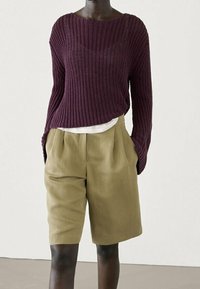 Bordowy sweter z dzianiny o szerokim dekolcie, zestawiony z khaki spodniami krótkimi na miarę, z przednimi plisami i bocznymi kieszeniami.