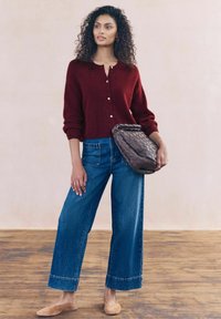 Burgunderfarvet uld cardigan med knapper, parret med brede blå denim jeans. Holder en struktureret, vævet brun taske. Beige flade sko fuldender looket.