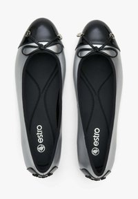 Czarne lakierowane baleriny z okrągłym noskiem, detalem w postaci kokardki oraz czarnym wnętrzem. Posiadają elastyczne wykończenie i logo na wkładce.