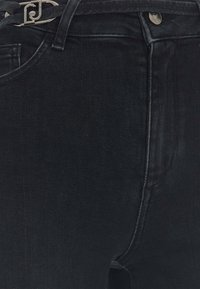 Jeans neri in denim con una vestibilità slim, caratterizzati da una superficie liscia, cuciture a macchina e una chiusura con bottone metallico.