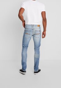 Ljusblå denimjeans med slim fit, som har bakfickor och en brun läderlappar vid midjan. Texturerad tyg med urtvättning.