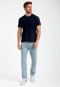 T-shirt a maniche corte blu navy con scollatura rotonda, abbinato a jeans blu chiaro. Il modello indossa sneakers bianche e ha un tessuto testurizzato.