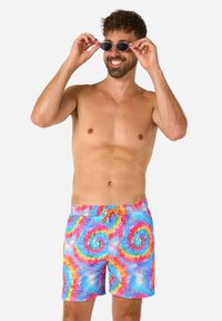 Peldbikses ar spilgtu tie-dye rakstu zilo, rozā un dzeltenajā krāsā, ar oranžu saiti un brīvu piegriezumu.