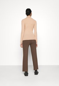 Beige ribbad långärmad topp kombinerad med bruna högmidjade utsvängda byxor. Modellen visas bakifrån, iförd svarta ankelboots.