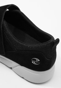 Chaussure en daim noir avec une tige en tissu extensible et texturé, dotée d'un détail de logo et d'une semelle en caoutchouc blanche contrastante.