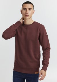 Burgundská mikina s okrúhlym výstrihom, rebrovanými manžetami a spodným krajom, s textúrovanou tkaninou a koženou nášivkou s logom na ľavom rukáve.
