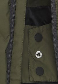 Olivgrön jacka med foder som har ficka, med en svart dragkedja och runda svarta och silverfärgade tryckknappar för säker stängning.