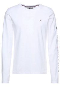 Vit långärmad tröja med rundad hals och liten Tommy Hilfiger-flagglogga på bröstet, samt märkesnamnet tryckt vertikalt på vänster ärm.