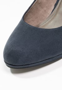 Gros plan sur l'avant d'une chaussure plate en daim bleu foncé avec un bout arrondi et une semelle intérieure beige coussinée.