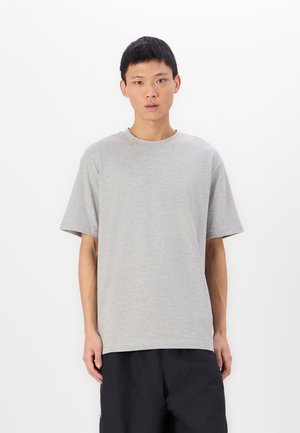 Gray short-sleeve t-shirt made of cotton with a round neck and relaxed fit, worn by a person against a plain white background.
