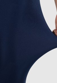 Mörkblå elastisk tyg, slät textur, närbild av en hand som drar i materialet och visar dess elasticitet och mjukhet.