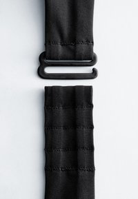 Deux sangles en tissu élastique noir avec bords cousus, dont une attachée à une boucle en plastique noire à double boucle, sur fond blanc.