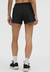 Shorts de sport negre cu talie elastică medie, având o textură netedă și un design minimalist. Completează ținuta cu adidași negri și șosete albe.