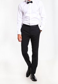 Zwarte dress pants met een slim fit, gecombineerd met een witte overhemd met knopen en een zwarte strik. Glanzende zwarte dresschoenen maken de outfit af.