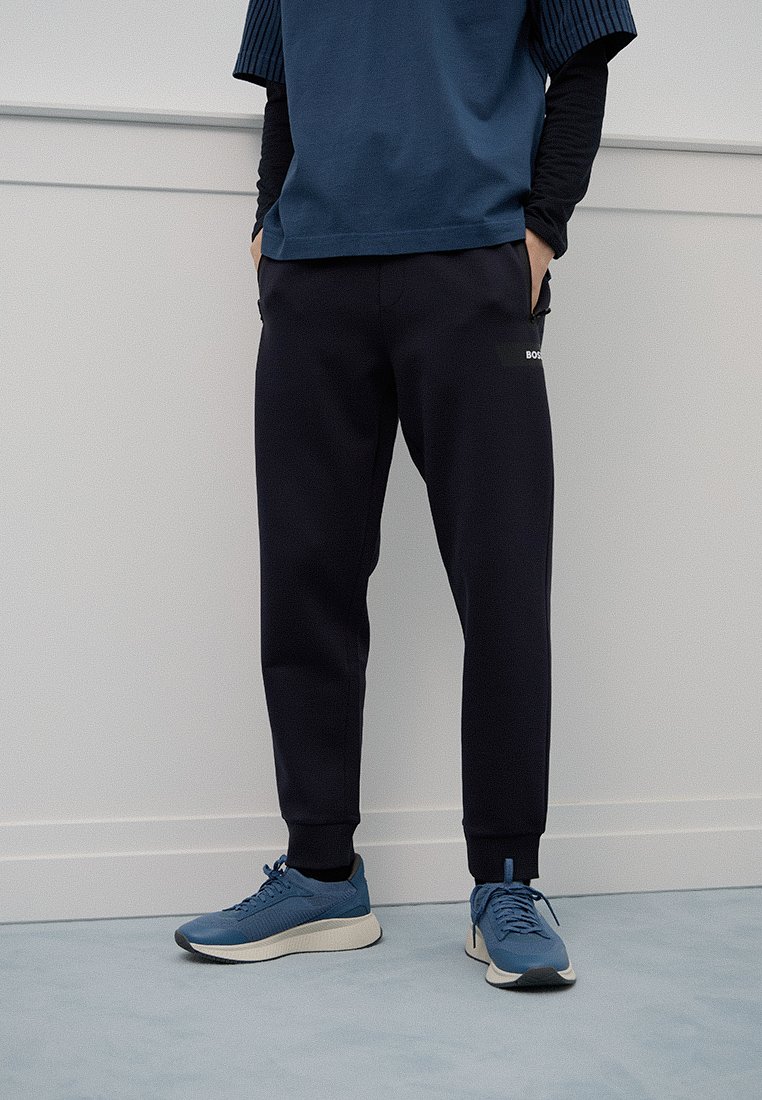 Marineblauwe joggers met elastische boorden en zijzakken, gecombineerd met een blauwe sportshirt en bijpassende sneakers met een textuurpatroon.
